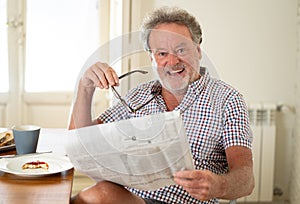 Happy old man reading the newspaper while having breakfast