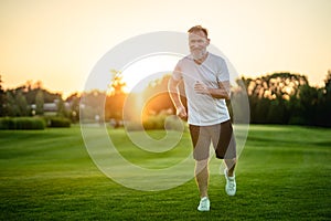 The happy old man running on the grass on the sunny background.