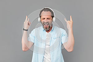 Happy old man sing song listening to rock music in headphones and making horn signs, rocker