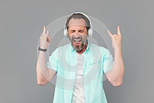 Happy old man sing song listening to rock music in headphones and making horn signs, rocker