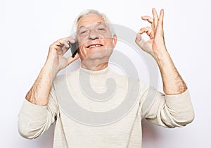 happy old man using smartphone and show ok desture over white background.