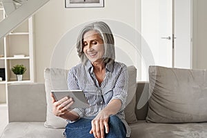 Happy old woman using digital tablet having virtual online meeting at home.