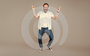 Happy old rocker sing along rock music playing in headphones making horn signs grey background, song
