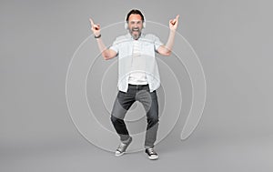 Happy old rocker sing along rock music playing in headphones making horn signs grey background, song