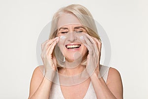 Happy old woman apply anti aging cream isolated on background