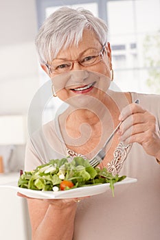 Happy old woman eating green salad