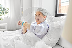 happy old woman with health tracker sitting in bed