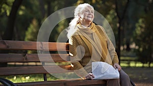 Happy old woman reading newspaper, sitting on bench in park, retirement age
