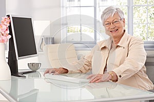 Happy old woman using computer at home