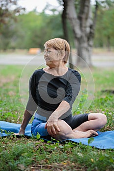 Happy old yoga woman. Smiling mature lady on a mat on a park background. Healthy lifestyle concept. Copy space.