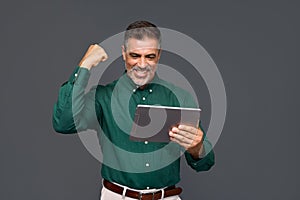Happy older business man investor looking at digital tablet winning online.