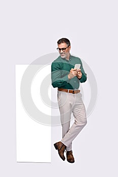 Happy older business man standing near big phone mockup using smartphone.