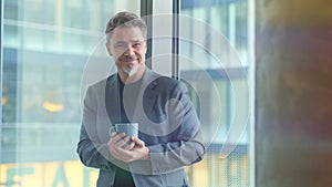 Happy older businessman taking break in office drinking coffee, thinking.