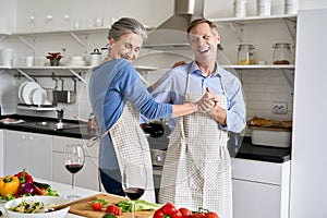 Happy older couple dancing in kitchen preparing healthy meal, having fun.