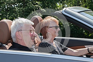 Happy older couple drives with a luxury convertible car