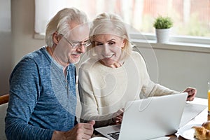 Happy older family couple talking using laptop having breakfast