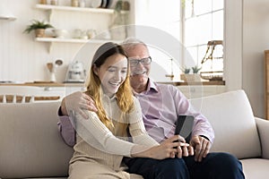 Happy older grandfather and teen granddaughter child using digital gadget