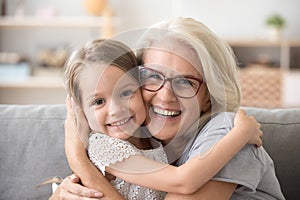 Happy older grandmother hugging little grandchild girl looking a photo