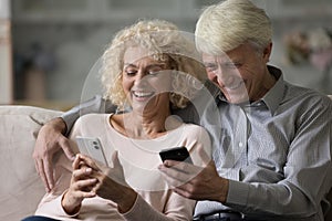 Happy older husband and wife holding smartphone, reading messages
