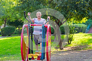 Happy older man working out on the sports public equipment in the outdoor gym.