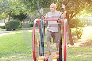 Happy older man working out on the sports public equipment in the outdoor gym. SportivE man doing physical exercise.