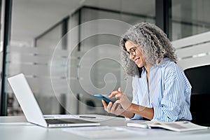 Happy older mature business woman using mobile phone working in office.