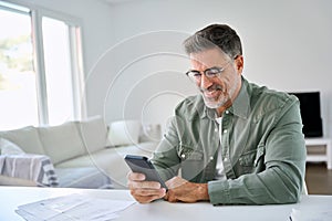 Happy older mature man using mobile cell phone at home in living room.
