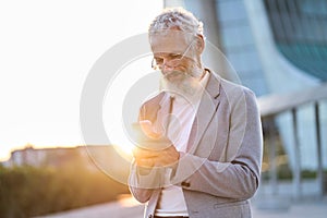Happy older professional business man holding phone using cellphone outdoor.