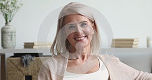 Happy older middle aged woman looking at camera at home