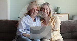 Happy older mom adult daughter sit on sofa with laptop