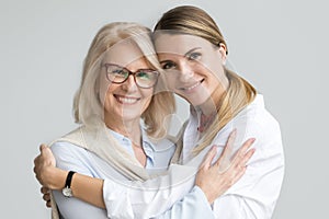 Happy older mother and adult daughter embracing looking at camer