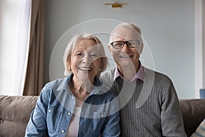 Happy older retired husband and wife sitting on home couch