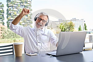 Happy older senior business man using laptop celebrating result winning online.