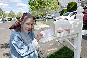 Happy older senior citizen woman smiles as she removes a blank white envelope from a white mailbox