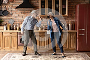 Happy older senior loving family couple singing songs in kitchen.