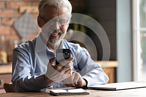 Happy older senior retired man in glasses looking at smartphone screen.