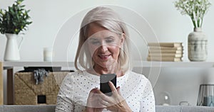 Happy older woman using phone mobile apps sit on couch