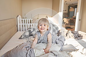 A happy one-and-a-half-year-old girl helps and has fun and smiles while in a bright apartment. change of bed linen
