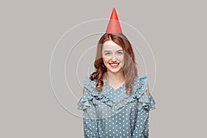 Happy optimistic beautiful girl in ruffle blouse and funny party hat looking at camera, smiling enjoying birthday