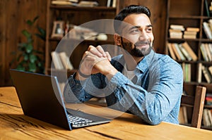 Happy and optimistic Indian man in casual wear using laptop