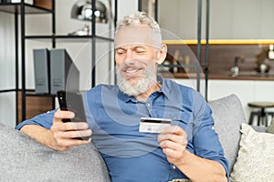 Happy optimistic mature man holding smartphone and credit card