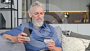 Happy optimistic mature man holding smartphone and credit card