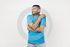 Happy optimistic smiling man hugging himself, looks satisfied, expressing happiness.