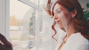 Happy optimistic young woman opening curtain lace looking through window.