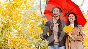 Happy ouple walking under umbrella at rainy autumn day