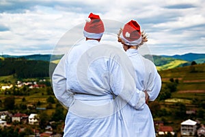 Happy Ñouple in a white coat and Santa Helper Hats on the mountain