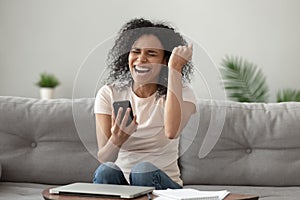 Happy overjoyed african woman holding mobile phone celebrating win