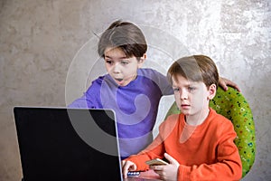 Happy overjoyed boy with his friend screaming excitedly, keeping fists pumped while playing video games on laptop pc, cheering