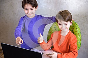 Happy overjoyed boy with his friend screaming excitedly, keeping fists pumped while playing video games on laptop pc, cheering