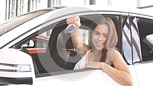 Happy overjoyed brunette female new car owner sitting in white car and demonstrates the key